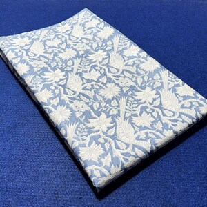 Könnte beinhalten: Ein blauer Stoff mit einem weißen Blumenmuster mit Vögeln. Der Stoff fühlt sich weich und strukturiert an.