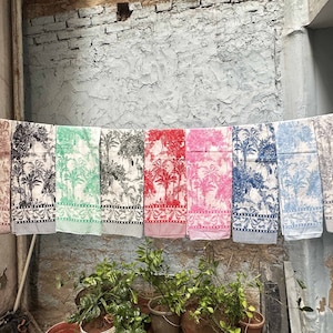 以下が含まれることがあります： ヤシの木の模様がついたカラフルなタオルが8枚、物干し竿にかけられています。タオルの色はピンク、赤、緑、青、グレーです。