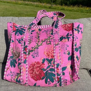 May include: A pink quilted tote bag with a floral print. The bag has two straps and a white and pink trim.