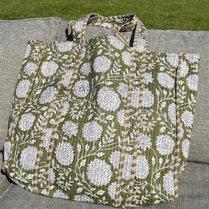 May include: A green quilted tote bag with a white floral pattern and brown stripes. The bag has two handles.
