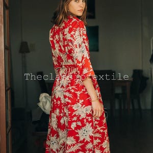 May include: A woman wearing a red and white floral midi dress with a tie waist. The dress has a side slit and is made of a lightweight fabric.