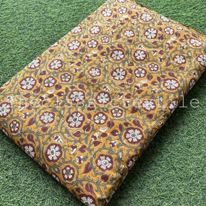 Może przedstawiać: Żółty bawełniany materiał w kolorze musztardowym z powtarzającym się wzorem kwiatowym w odcieniach bordowego, białego i zielonego.