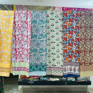 Pode incluir: Seis painéis de tecido diferentes com padrões florais em várias cores, incluindo amarelo, vermelho, azul, verde e marrom. Os painéis estão pendurados em um rack em uma loja.