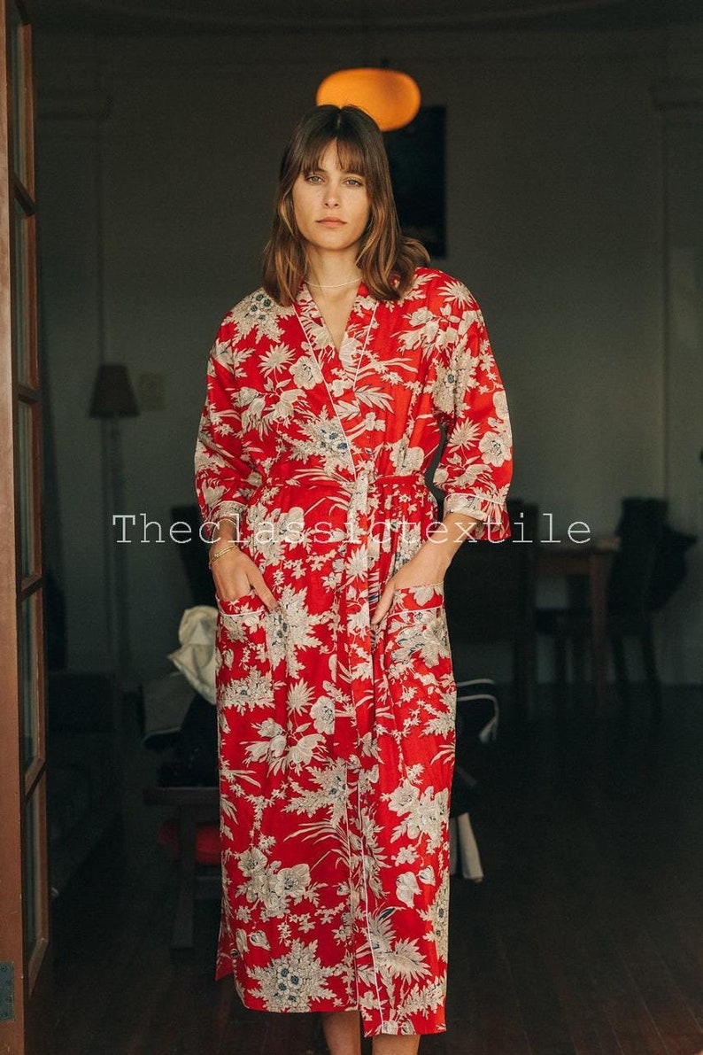 May include: A red and white floral print robe with long sleeves and a sash tie. The robe has a white trim and pockets.