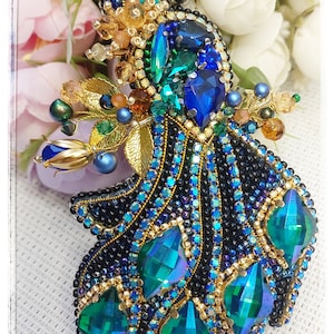 May include: A beaded peacock brooch with a blue and green iridescent design. The peacock's tail feathers are made of black and blue beads with green and gold accents.