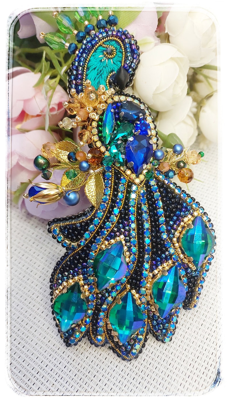 May include: A beaded peacock brooch with a blue and green iridescent design. The peacock's tail feathers are made of black and blue beads with green and gold accents.