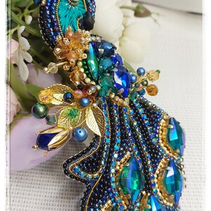 May include: A beaded peacock brooch with iridescent green and blue stones, gold accents, and black beads.