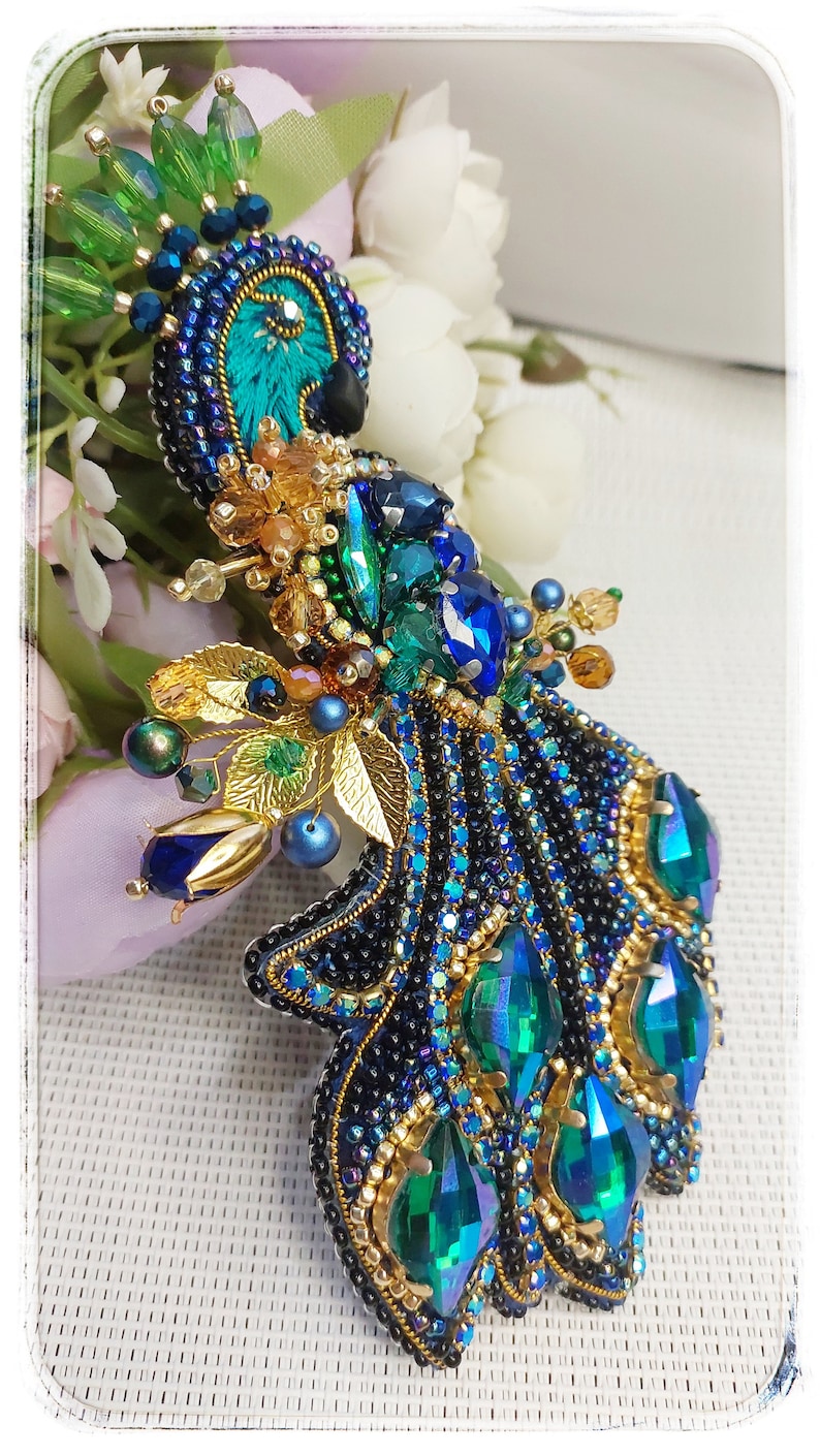 May include: A beaded peacock brooch with iridescent green and blue stones, gold accents, and black beads.