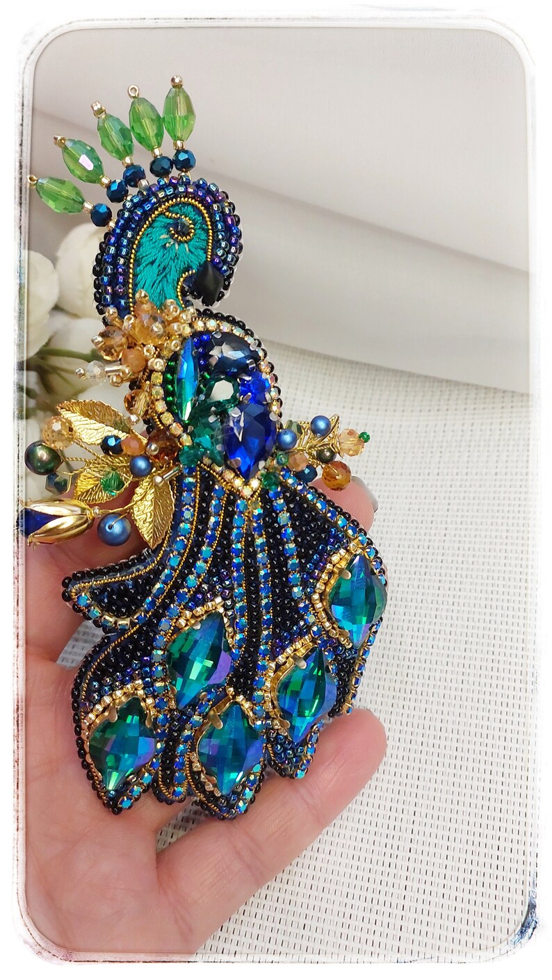 May include: A beaded peacock brooch with blue, green, and gold accents. The peacock's tail feathers are made of iridescent green and blue beads.