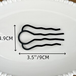 May include: A black hair comb, 3.5 inches (9 cm) wide and 2 inches (4.9 cm) tall, with a unique design. The comb features a curved, wavy pattern. It is displayed on a white oval plate.