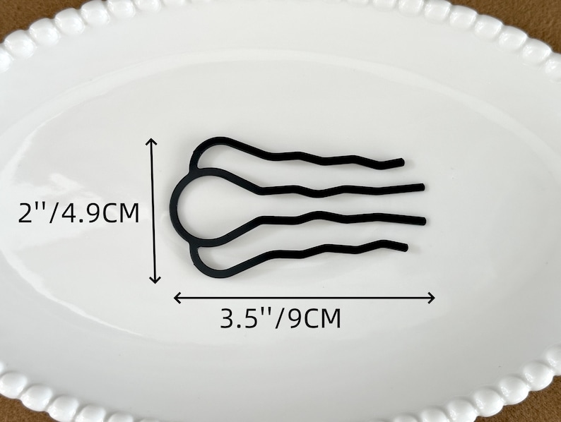 May include: A black hair comb, 3.5 inches (9 cm) wide and 2 inches (4.9 cm) tall, with a unique design. The comb features a curved, wavy pattern. It is displayed on a white oval plate.