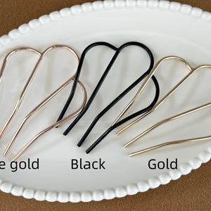 May include: Hair accessories in rose gold, black, and gold. The metal hair pins are arranged on a white oval plate. The text "Rose gold", "Black", and "Gold" are below the hair pins.