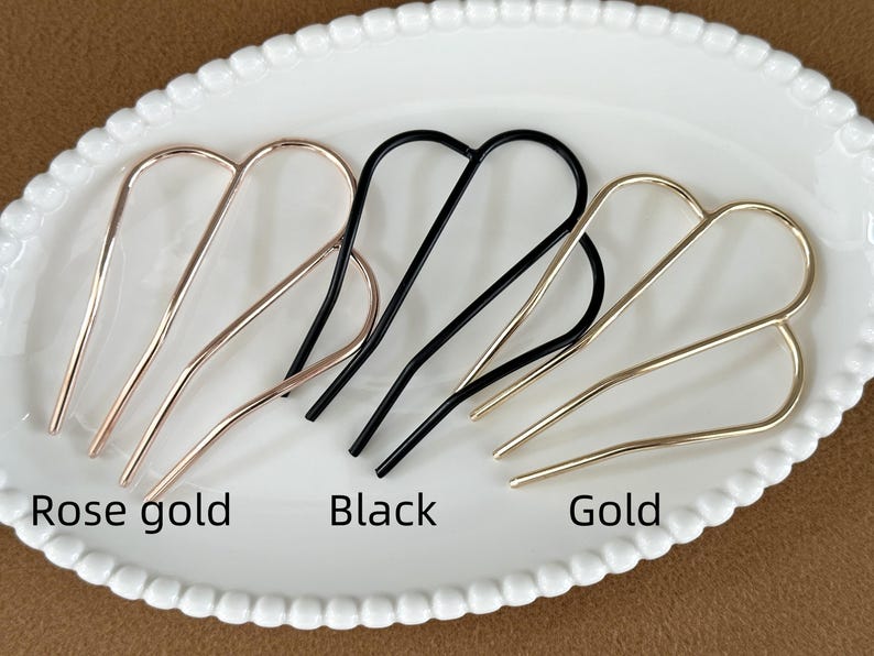 May include: Hair accessories in rose gold, black, and gold. The metal hair pins are arranged on a white oval plate. The text "Rose gold", "Black", and "Gold" are below the hair pins.