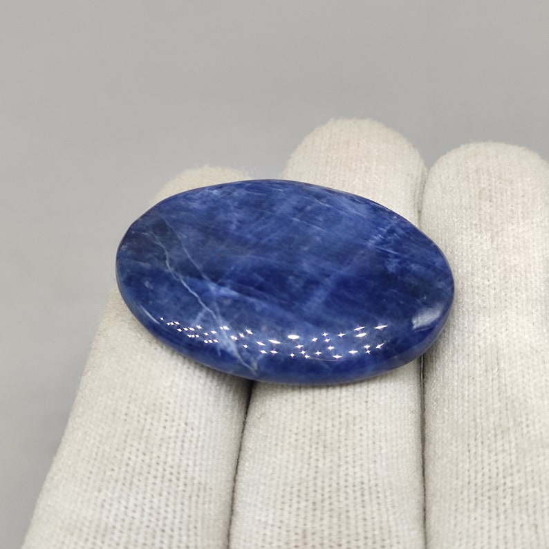 May include: A smooth, oval-shaped blue sodalite stone with white veining. The stone is polished and has a glossy finish.