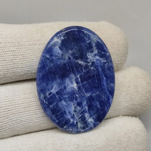 May include: A smooth, oval-shaped blue sodalite cabochon with white veining. The stone has a polished finish and is a deep blue color.