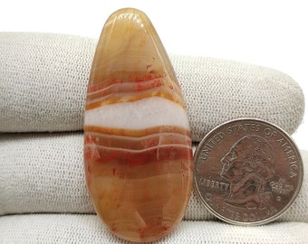 May include: A teardrop-shaped agate pendant with red, white, and brown banding. The pendant is approximately the size of a US quarter.