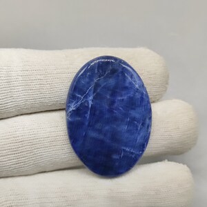 May include: A smooth, oval-shaped cabochon of blue sodalite with white veining. The stone has a polished finish and is a deep blue color.