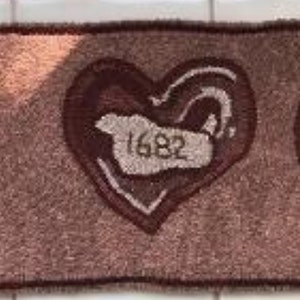 May include: A brown rug with three large, stylized hearts. The center heart has the number "1682" embroidered inside.