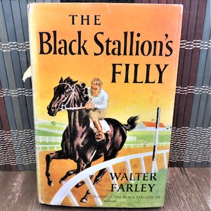 Puede incluir: Una portada de libro vintage con un caballo negro corriendo en una pista con un jinete montando. El t&iacute;tulo es "The Black Stallion's Filly" de Walter Farley, autor de "The Black Stallion".