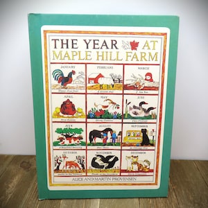 May include: A hardcover book titled The Year at Maple Hill Farm by Alice and Martin Provensen. The green cover features a grid of twelve illustrated panels, each depicting a different month of the year with animals, seasonal scenes, and text.