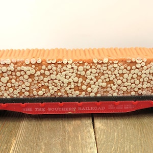 May include: A model train car, painted black, red, and orange, filled with small, round, white and orange objects. The words "THE SOUTHERN RAILROAD" are printed on the side of the car.
