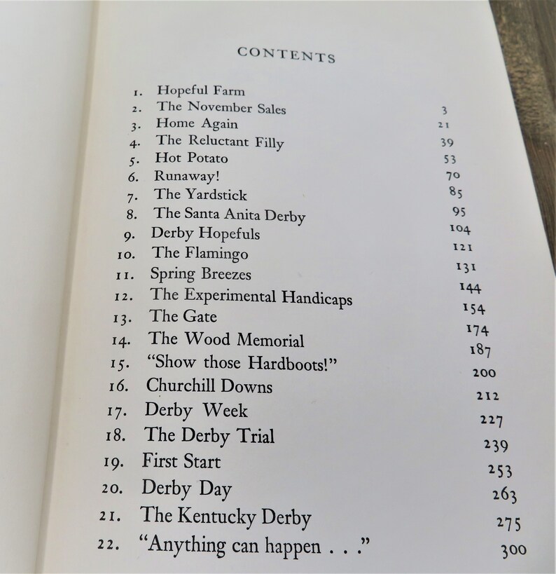 Puede incluir: Un libro titulado "CONTENTS" con una lista de cap&iacute;tulos y n&uacute;meros de p&aacute;gina. Los cap&iacute;tulos incluyen "Hopeful Farm", "The November Sales", "Home Again", "The Reluctant Filly", "Hot Potato", "Runaway!", "The Yardstick", "The Santa Anita Derby", "Derby Hopefuls", "The Flamingo", "Spring Breezes", "The Experimental Handicaps", "The Gate", "The Wood Memorial", "Show those Hardboots!", "Churchill Downs", "Derby Week", "The Derby Trial", "First Start", "Derby Day", "The Kentucky Derby" y "Anything can happen..."