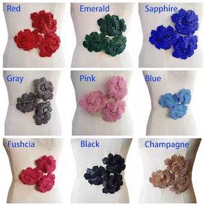 Può includere: Una collezione di applicazioni floreali con perline in vari colori, tra cui rosso, verde smeraldo, blu zaffiro, grigio, rosa, blu, fucsia, nero e champagne. Ogni applicazione presenta un gruppo di fiori, esposte su un manichino.