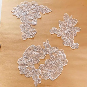 Peut inclure: Trois appliques en dentelle blanche avec des motifs floraux. Les appliques sont sur un fond brun.