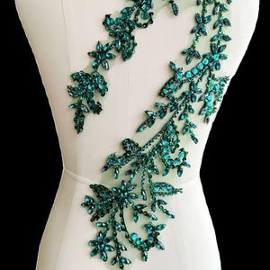 以下が含まれることがあります： 透き通ったメッシュ生地に、ターコイズグリーンのフローラルモチーフのアップリケが施されています。ラインストーンとスパンコールが輝きを添え、どんな衣服にも華やかさをプラスします。