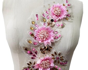 Puede incluir: Aplique floral rosa con lentejuelas y cuentas doradas y rosas. El aplique está sobre un fondo blanco.