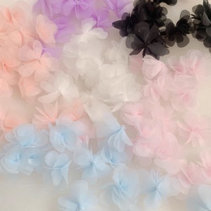 Può includere: Una varietà di passamanerie di fiori in tessuto trasparente in diversi colori, tra cui azzurro, rosa, bianco e viola. I fiori sono sovrapposti e si sovrappongono, creando un look delicato e femminile.