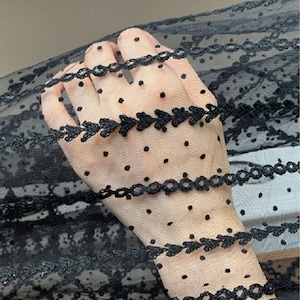 Può includere: Tessuto nero trasparente con motivo a pois e bordatura in pizzo nero. Il tessuto è delicato e ha una texture morbida e fluida.