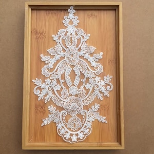 May include: White lace applique featuring a floral design. The lace is delicate and intricate, with a variety of shapes and sizes of flowers. The applique is ideal for adding a touch of elegance to any project.