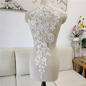 May include: White lace applique with a floral design. The lace is delicate and intricate, with small flowers and leaves. The applique is perfect for adding a touch of elegance to any garment.