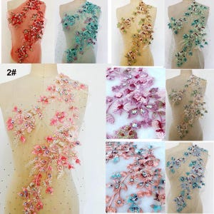 Puede incluir: Surtido de apliques florales con pedrería y cuentas en varios colores, incluyendo rosa, azul, verde y rojo. Los apliques están sobre una tela de malla transparente.