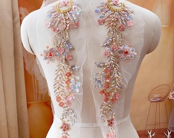 May include: Two delicate floral appliques with pink and gold embellishments on a white mesh background. The appliques feature intricate floral designs with sequins, beads, and pearls.