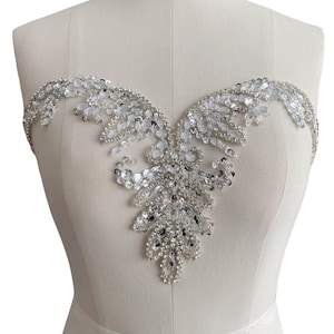 Peut inclure: Une embellissement en cristal argenté et transparent avec un design en forme de V. L'embellissement est fait de strass et de paillettes.