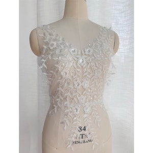 May include: White lace applique with sequins and floral designs. The applique is perfect for adding a touch of elegance to any garment.