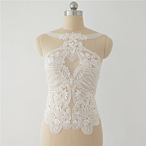 May include: White lace applique with a floral design and beaded accents. The applique is perfect for adding a touch of elegance to any garment.