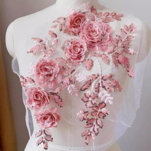 May include: Pink floral applique with sequins and beads. The applique features a cluster of roses and leaves.