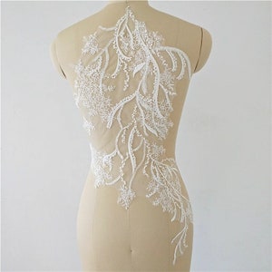 May include: White lace applique with beaded details. The lace features a floral design with delicate branches and leaves. This applique is perfect for adding a touch of elegance to any garment.