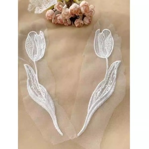 May include: Two white embroidered tulle fabric appliques featuring a tulip design. The appliques are perfect for adding a touch of elegance to clothing, accessories, or home decor projects.