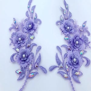 May include: Two lavender floral appliques with iridescent rhinestones and pearl accents. The appliques are ideal for adding a touch of elegance to clothing, accessories, or home decor.