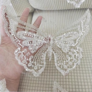 Può includere: Applique a forma di farfalla bianca con perline, dal design delicato. L'applique è realizzata con piccole perline e paillettes bianche ed è perfetta per aggiungere un tocco di eleganza a qualsiasi progetto.