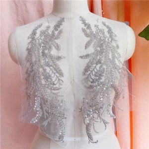 May include: Silver beaded lace applique with a floral design. The applique is on a sheer mesh fabric.