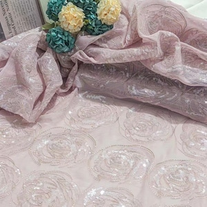 May include: Pale pink fabric with a delicate rose pattern made of sequins. The fabric is sheer and has a soft, flowing texture.