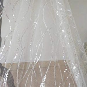 May include: White tulle fabric with silver sequins arranged in a pattern of curved lines.