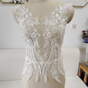 Puede incluir: Aplique de encaje blanco con adornos florales y de cuentas. El aplique presenta delicados diseños florales con cuentas nacaradas y lentejuelas.