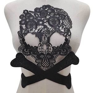 Könnte beinhalten: Schwarze Spitzenapplikation mit Totenkopf und gekreuzten Knochen. Der Totenkopf ist mit Blumenmustern verziert und die gekreuzten Knochen sind in der Mitte verbunden.