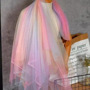 May include: Rainbow tulle fabric in shades of pink, blue, and yellow. The fabric is sheer and delicate, with a soft, flowing texture.